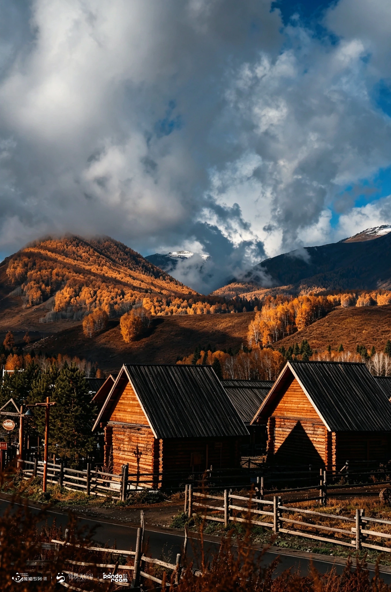 Wooden cabins behind a fence beneath autumn hills and dark cloud